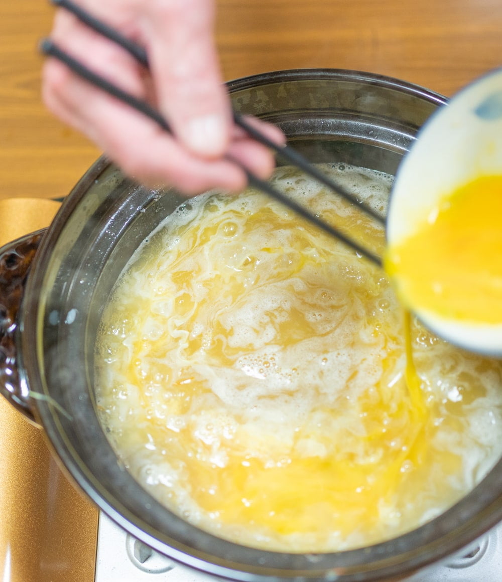 出汁が入った土鍋に卵液を回しかける