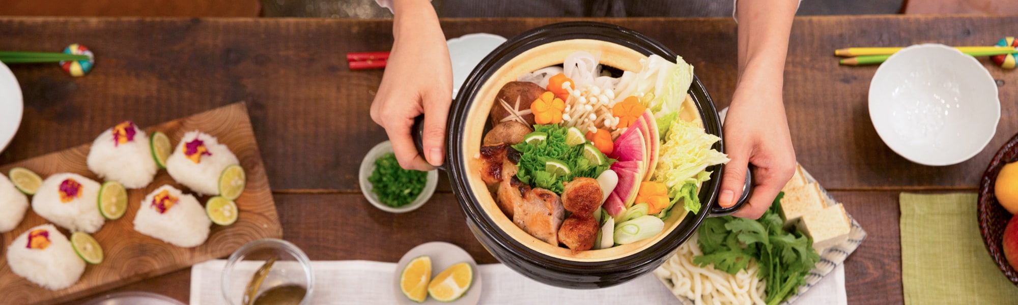 土鍋に椎茸、えのき、レモン、にんじん、ねぎ、かぶ、白菜が入った鍋と薬味とおにぎり