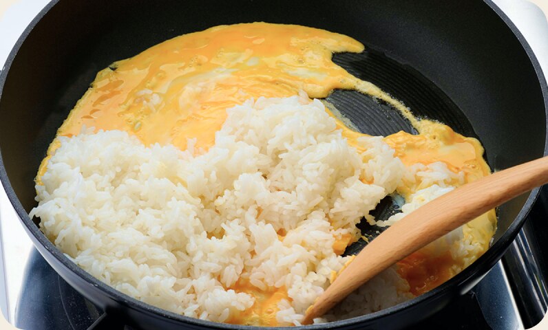 フライパンで半熟のたまごにごはんを加えているところ